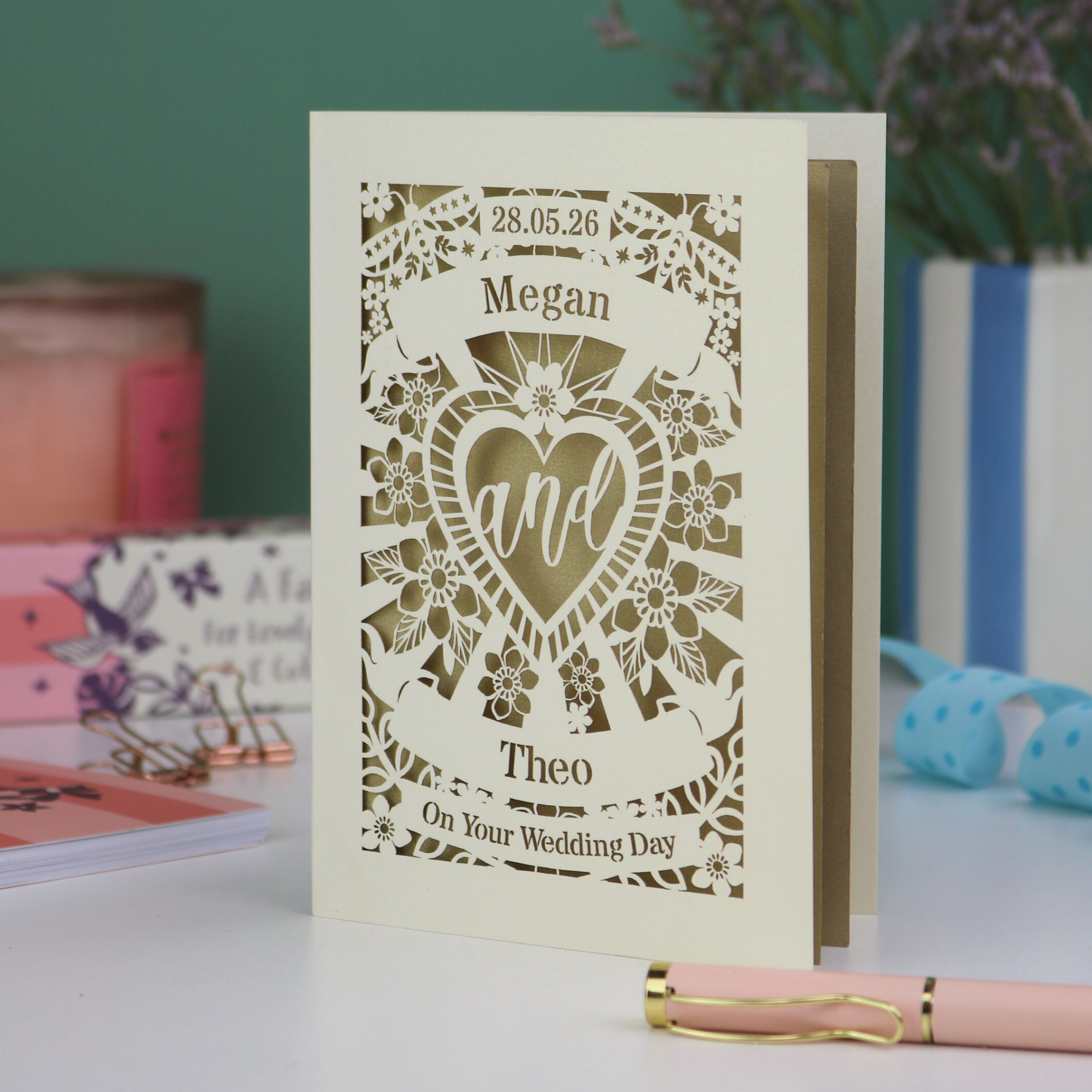 Personalised wedding card with laser-cut design and names 'Megan' and 'Theo' on a blurred background.