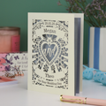 Personalised laser cut wedding card with decorative design and names on a table with candles and flowers in the background.