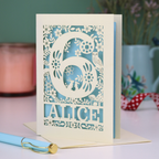 Laser cut 6th Birthday card with decorative number 6 and name 'Alice', and woodland design, on a table with a pen and plant in the background.