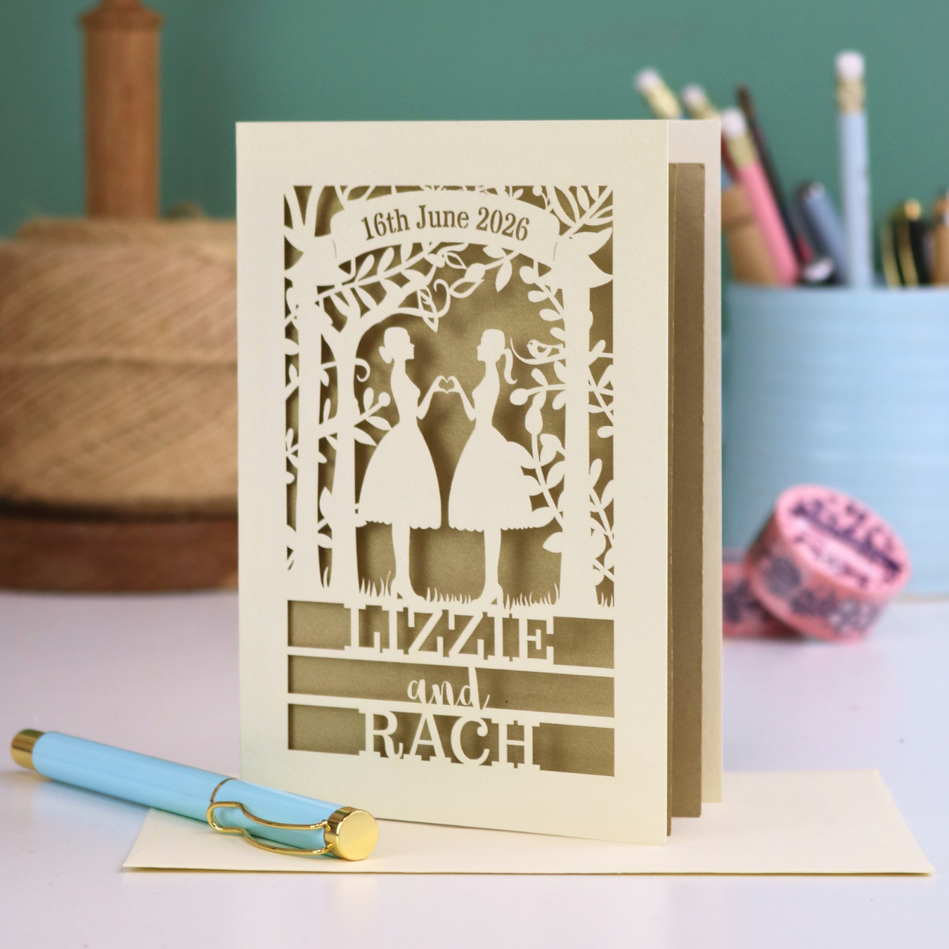 Personalized laser-cut lesbian anniversary card with cut-out silhouettes of a couple, text, and a pen on a desk.
