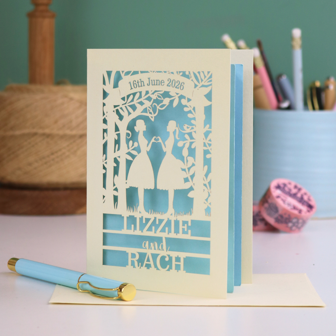 Personalized laser-cut lesbian anniversary card with cut-out silhouettes of a couple, text, and a pen on a desk.