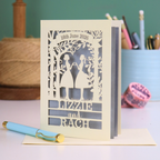 Personalized laser-cut lesbian anniversary card with cut-out silhouettes of a couple, text, and a pen on a desk.