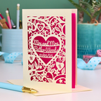 Laser-cut lesbian anniversary card with personalized text, 'Mrs and Mrs Butler-Woods, 01/05/25', surrounded by leaves and flowers,  on a desk with stationery items.