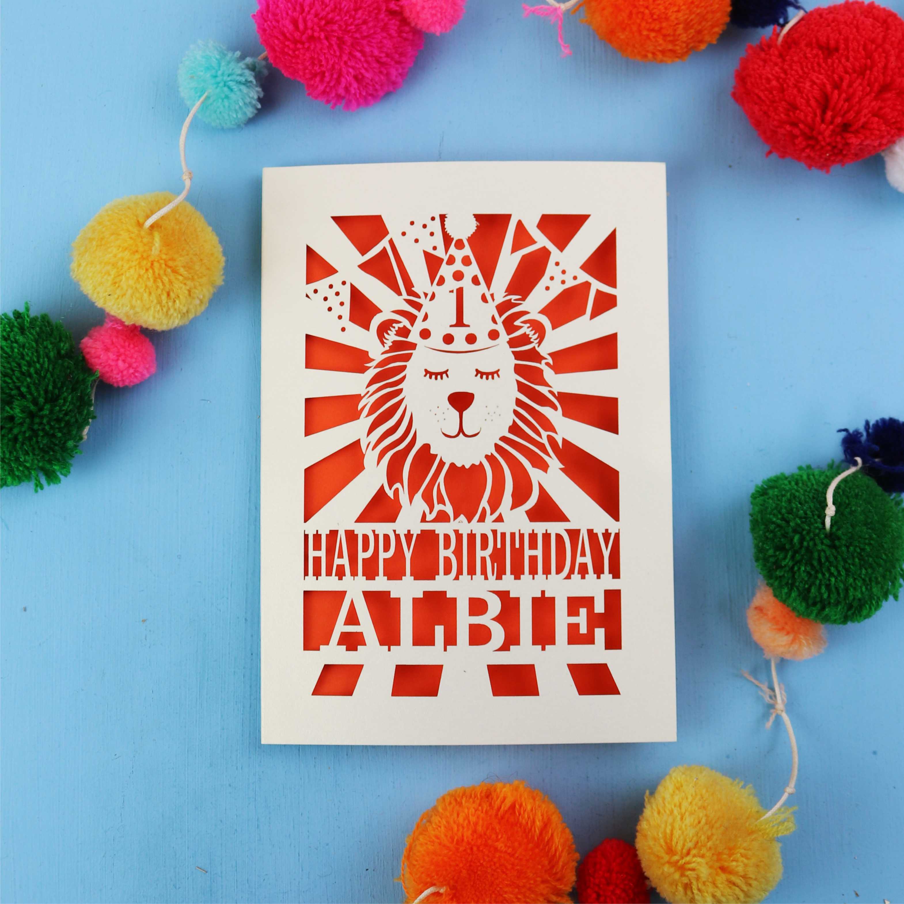 Special papercut 1st Birthday card with lion design and colourful pom-poms on a blue background