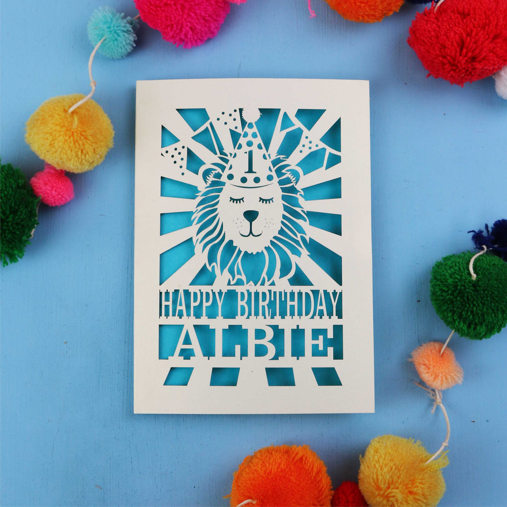 Keepsake 1st Birthday card with lion design and colourful pom-poms on a blue background