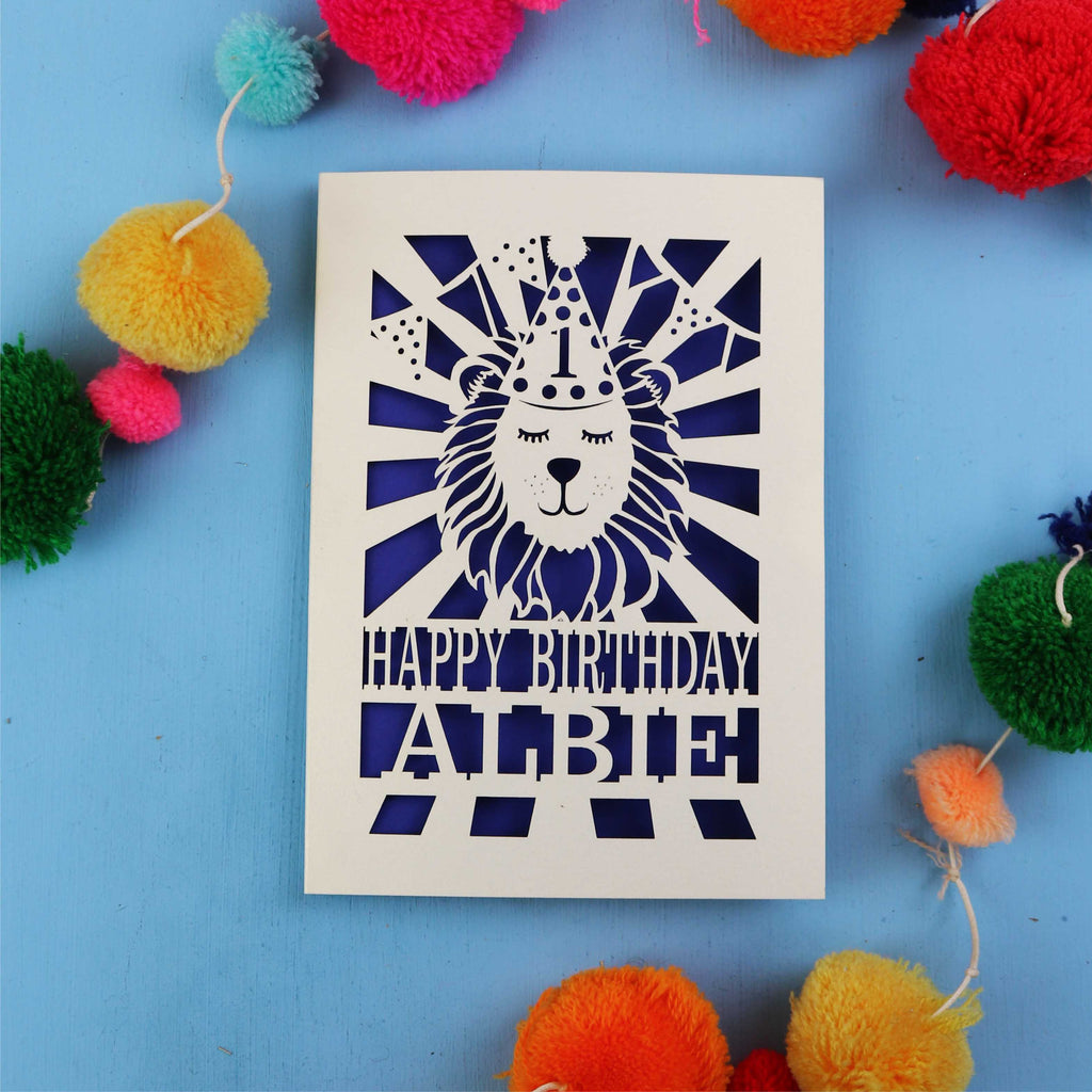 Beautiful 1st Birthday card with lion design and colourful pom-poms on a blue background