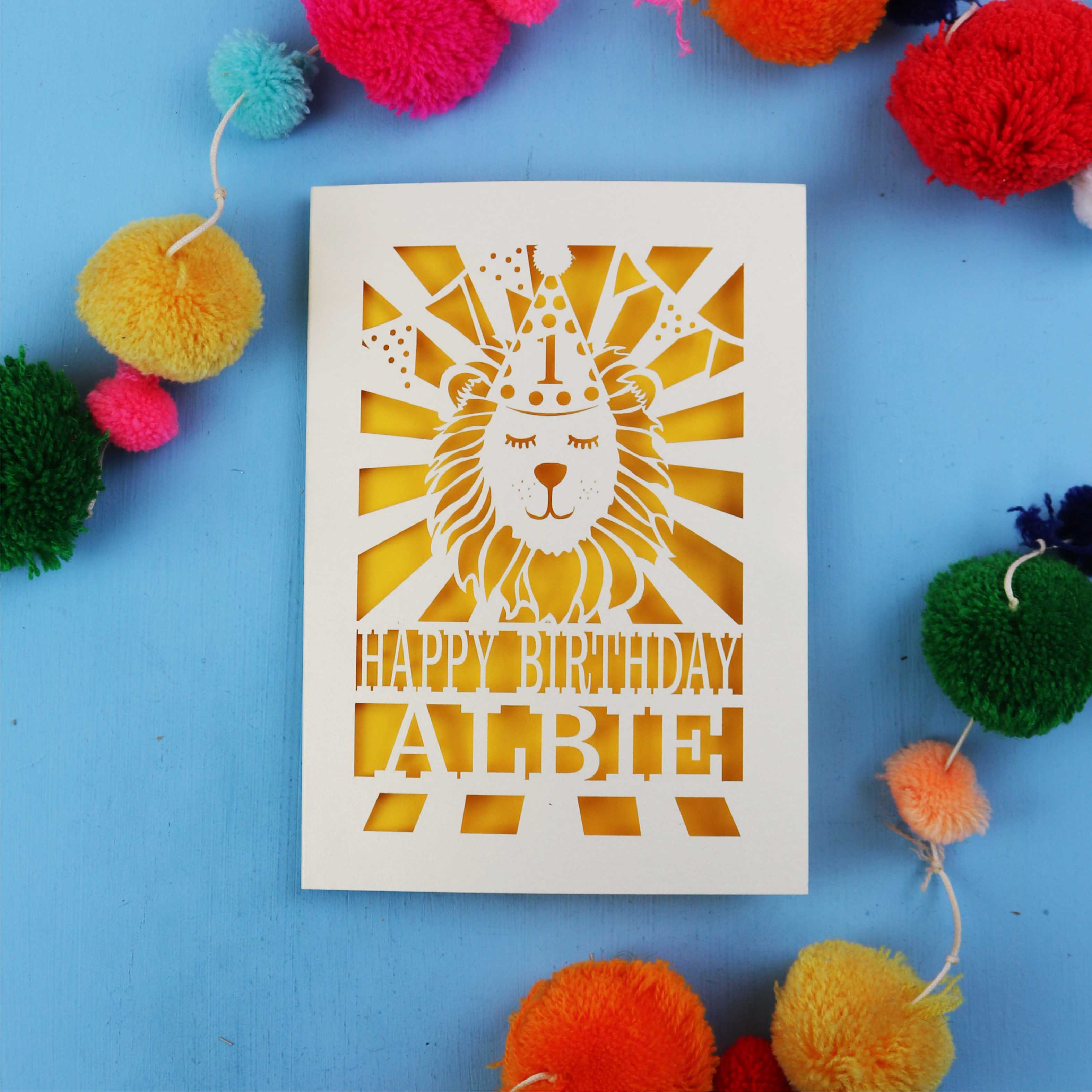Special first Birthday card with lion design and colourful pom-poms on a blue background