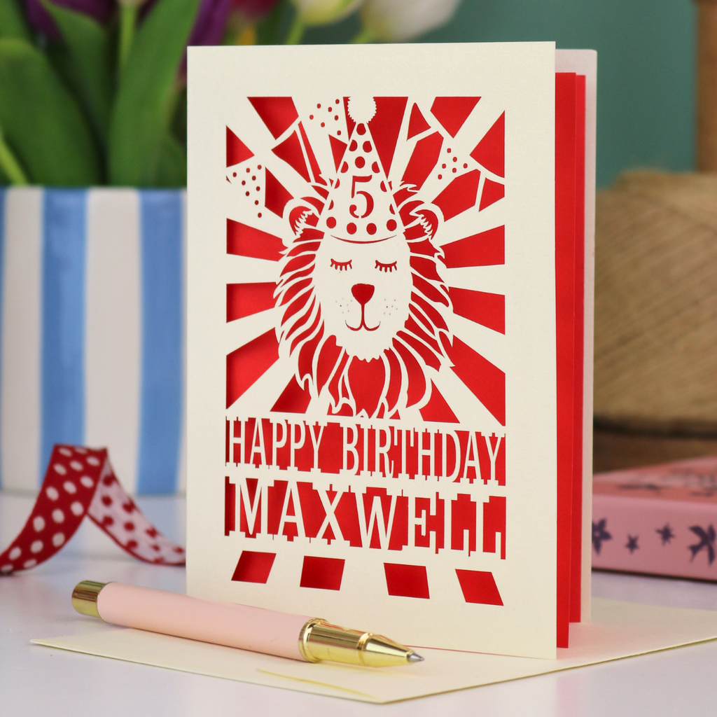 A laser cut kids' birthday card with cut out lion in a party hat, with text "Happy Birthday" and personalised with a name
