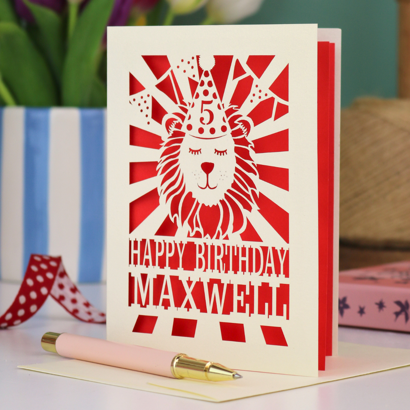 A laser cut kids' birthday card with cut out lion in a party hat, with text "Happy Birthday" and personalised with a name