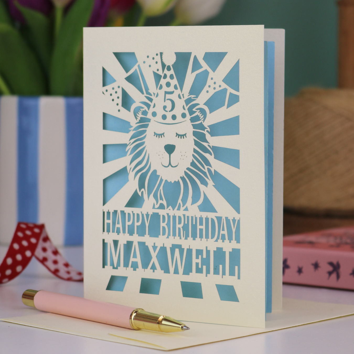 A laser cut kids' birthday card with cut out lion in a party hat, with text "Happy Birthday" and personalised with a name