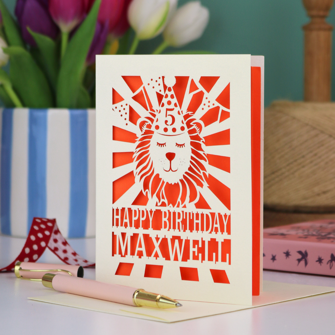 A laser cut kids' birthday card with cut out lion in a party hat, with text "Happy Birthday" and personalised with a name