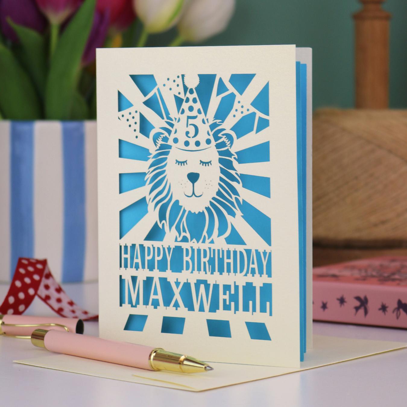 A laser cut kids' birthday card with cut out lion in a party hat, with text "Happy Birthday" and personalised with a name