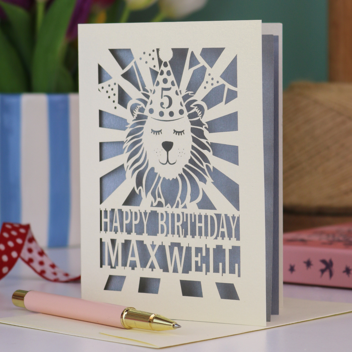 A laser cut kids' birthday card with cut out lion in a party hat, with text "Happy Birthday" and personalised with a name