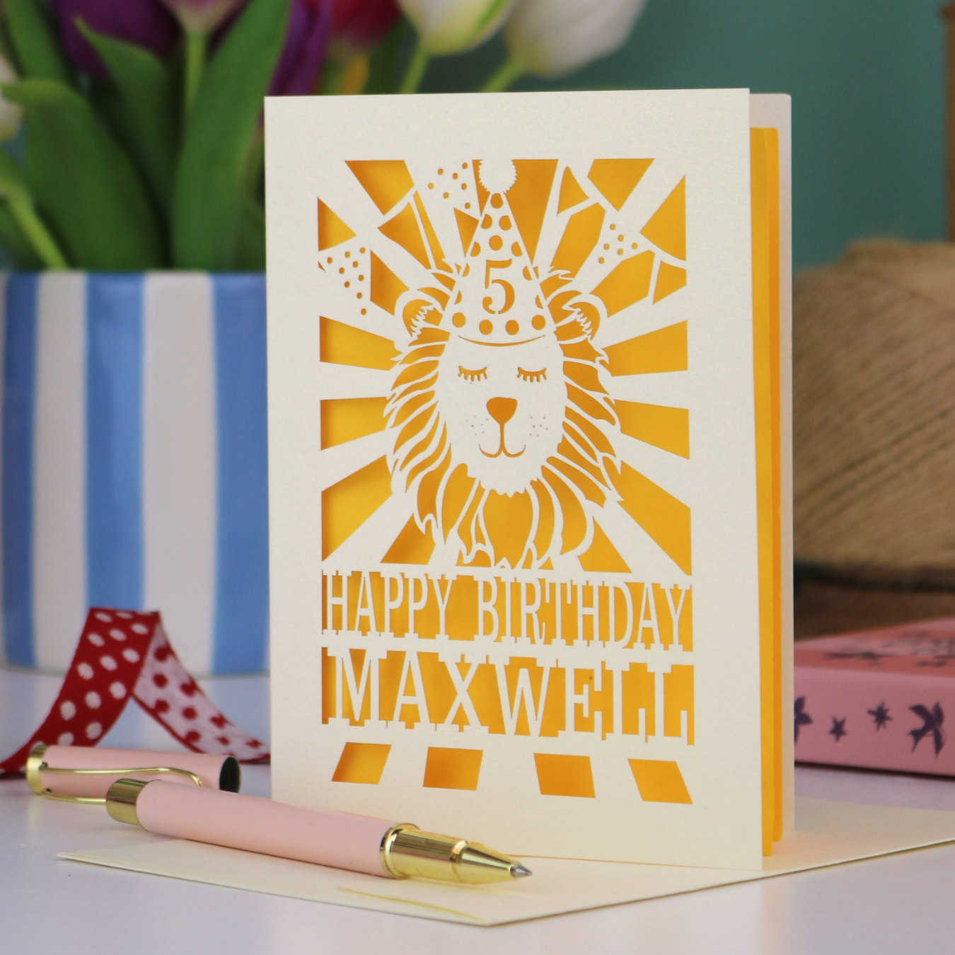 A laser cut kids' birthday card with cut out lion in a party hat, with text "Happy Birthday" and personalised with a name
