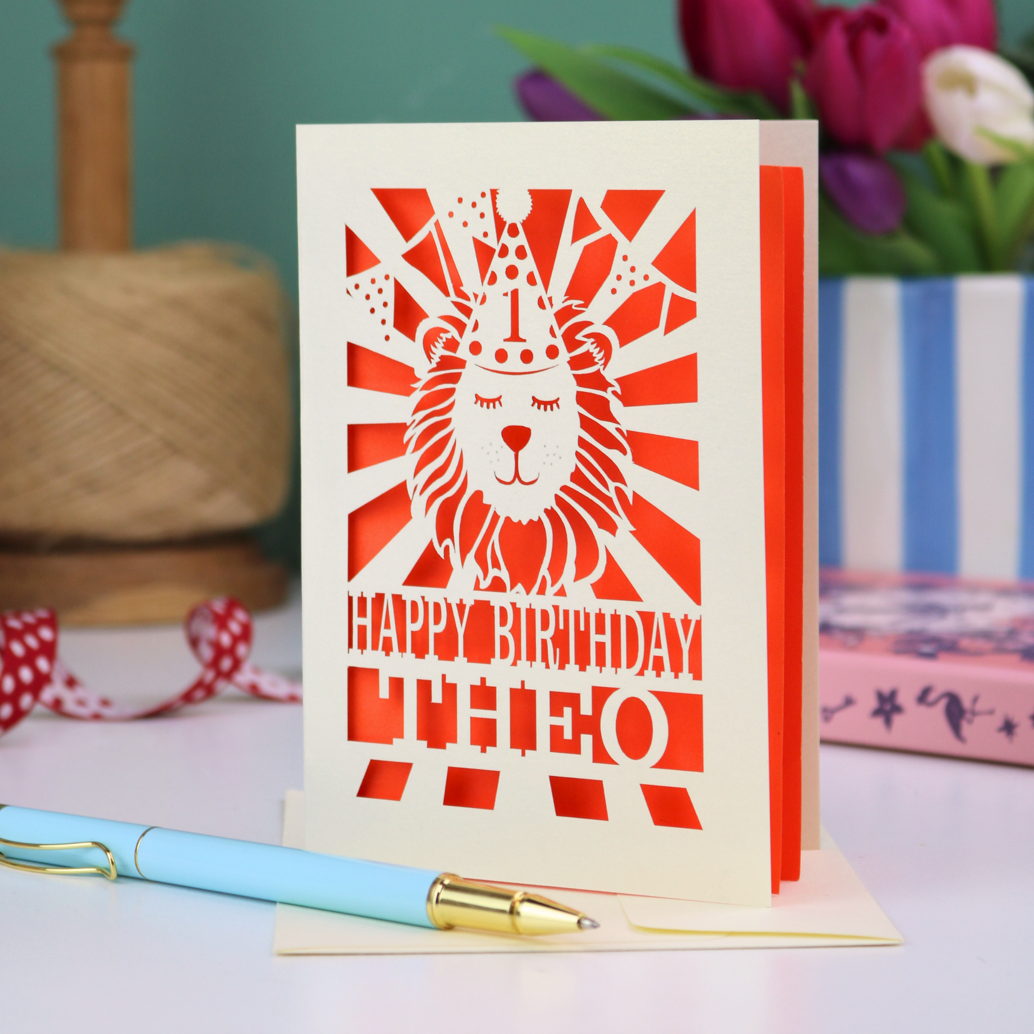 A personalised laser cut first birthday card with cut out design of a lion in a party hat, and text "Happy Birthday Theo"
