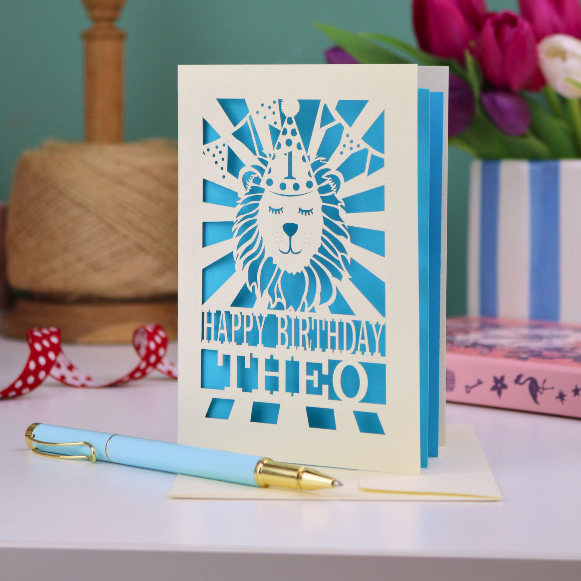 A personalised laser cut first birthday card for grandson, with cut out design of a lion in a party hat, and text "Happy Birthday Theo"