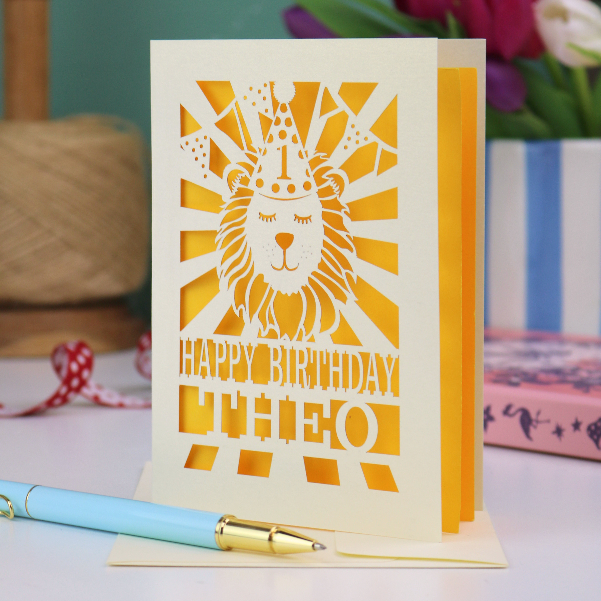 A personalised laser cut first birthday card for son, with cut out design of a lion in a party hat, and text "Happy Birthday Theo"