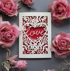 A paper cut engagement card with 'love' inside a floral heart design 