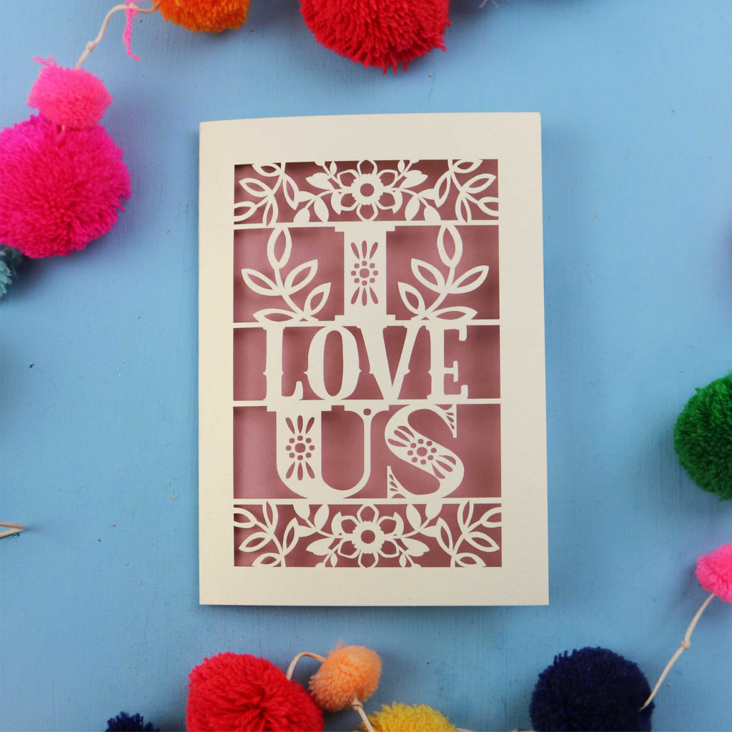 Decorative Valentine's Day card with 'I Love Us' text on a blue background with colourful pom-poms.