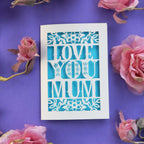 A cream cut out card for Mother's Day that says "Love you mum" and has a blue paper behind cut out design