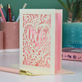 Luxury Greeting card with 'wife' in a heart design on a pink background, placed on a desk with stationery items.