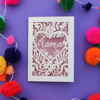 A cut out mother's day card with "mama" inside a heart surrounded by flowers and a dusky pink paper backing