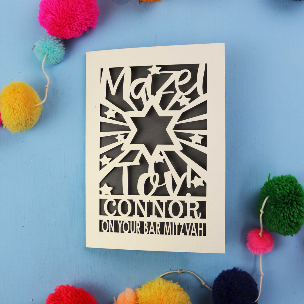 Decorative Bar Mitzvah card with cut-out text on a blue background with colourful pom-poms.
