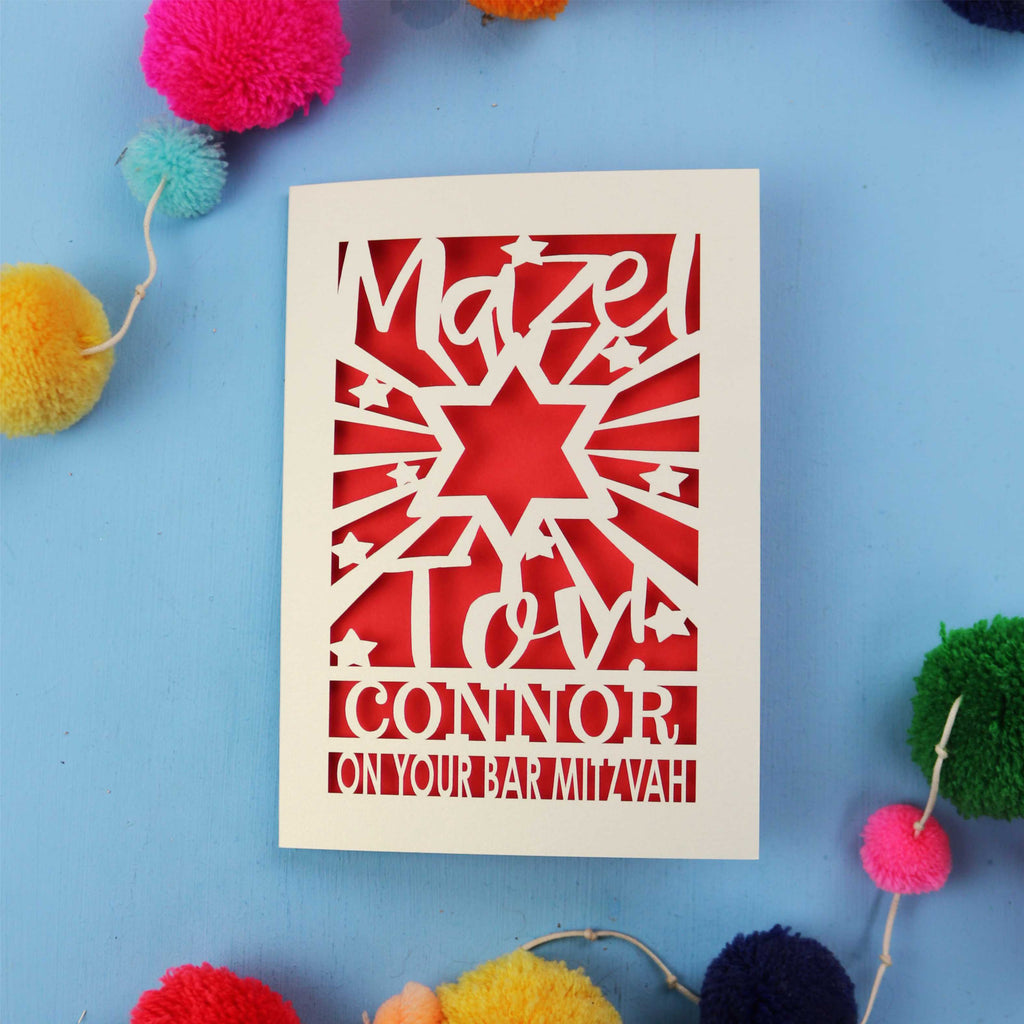Bar Mitzvah Card with cut-out design and text on a blue background with colourful pom-poms.