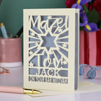 Decorative Laser cut Bar Mitzvah card with cut-out text, 'Mazel Tov Jack on your Bar mitzvah' on a table with stationery items.