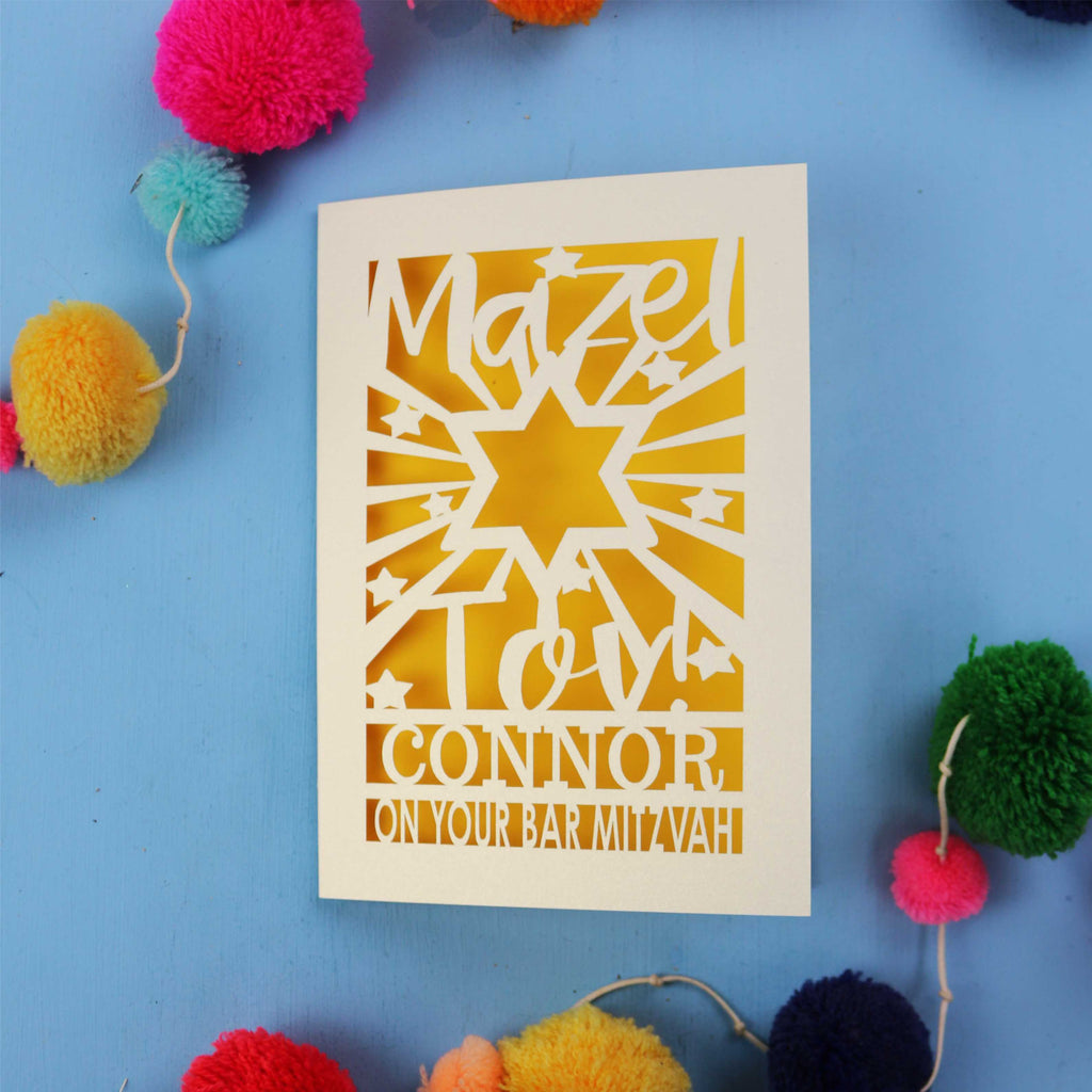 Bar Mitzvah Card with cut-out design and text on a blue background with colourful pom-poms.