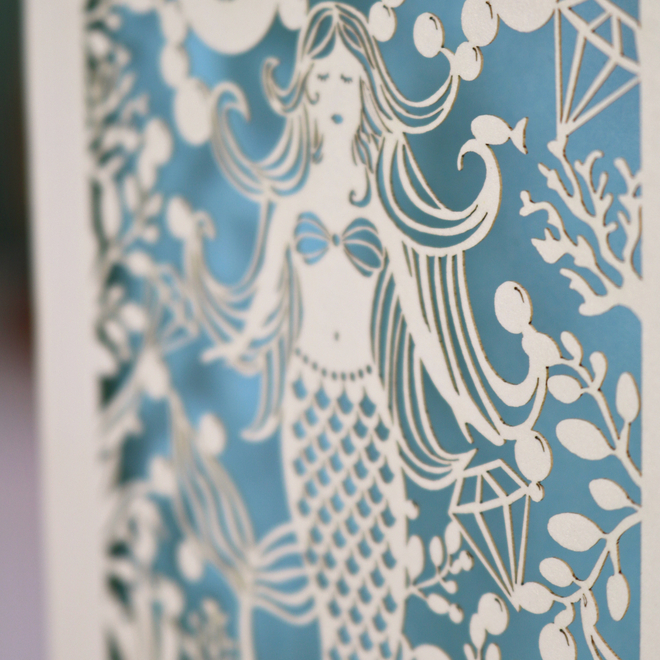 A laser cut mermaid birthday card, personalised with the age in cut out stencil font in a bubble, and the name across the bottom of the card. The design is a mermaid surrounded by bubbles, diamonds, fish and sea plants