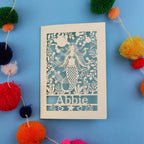 mermaid birthday card on a blue background surrounded by colourful pom-poms.
