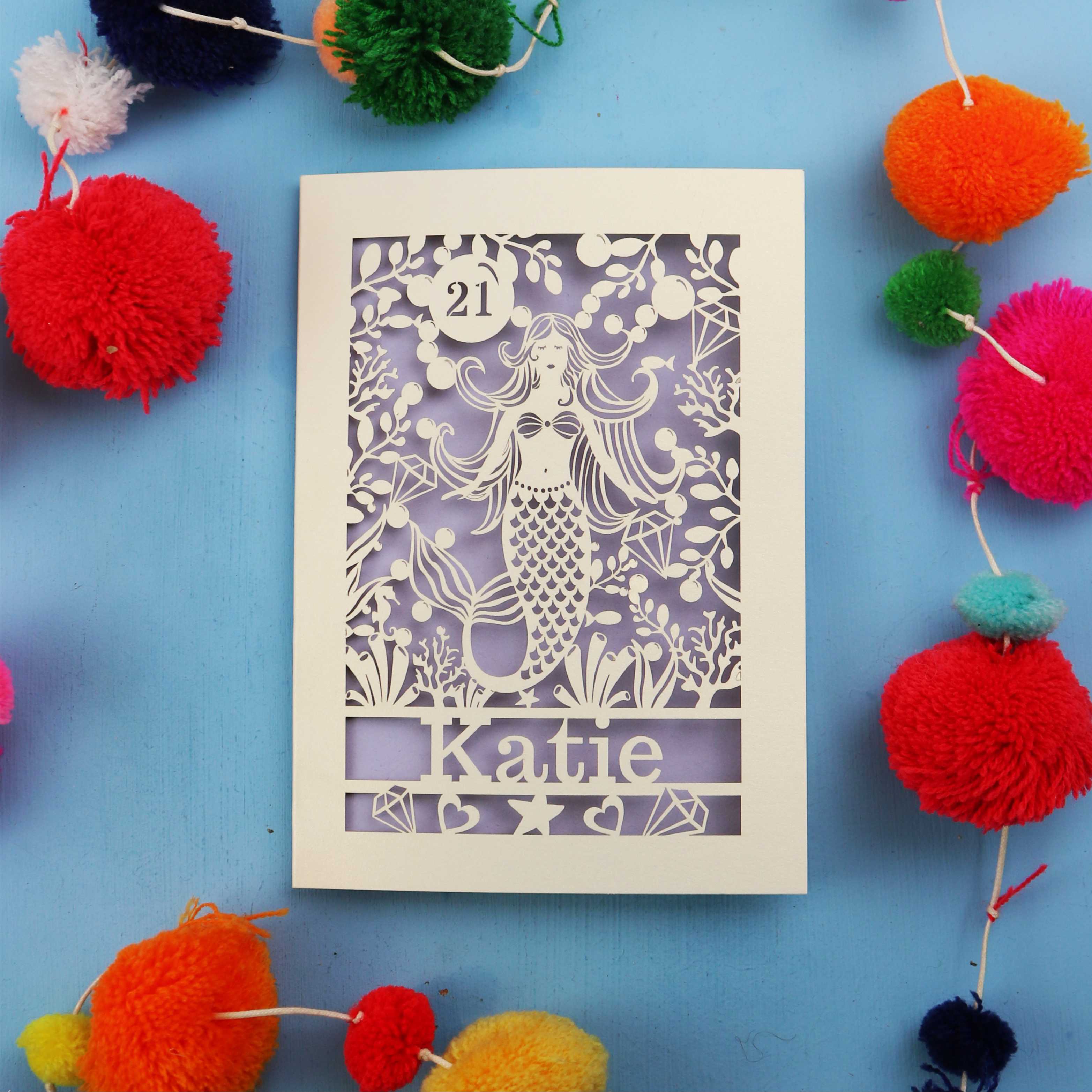 Decorative laser cut birthday card with mermaid design and colourful pom-poms on a blue background