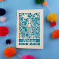 Paper cut out birthday card with a mermaid and 'Abbie' on a blue background surrounded by colourful pom-poms.