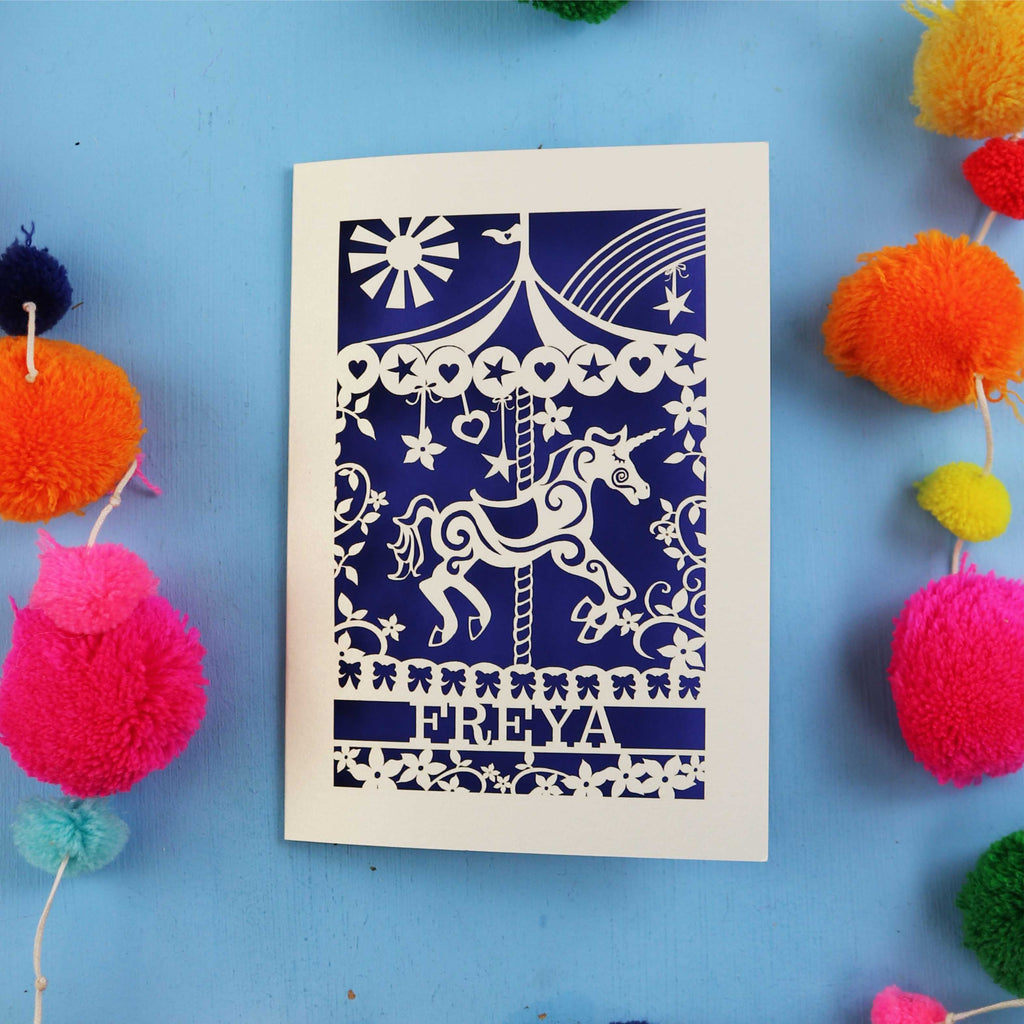 UK made Personalised birthday Card with carousel design and 'FREYA' text on a blue background with colourful pom-poms.