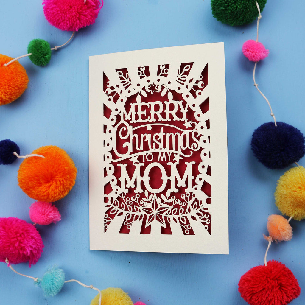Laser cut Mom Card with 'Merry Christmas to my Mom' text surrounded by colourful pom-poms on a blue background