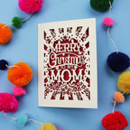Laser cut Mom Card with 'Merry Christmas to my Mom' text surrounded by colourful pom-poms on a blue background