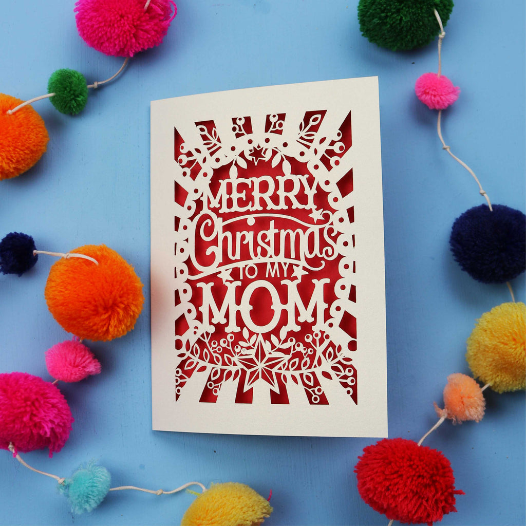 Laser cut Mom Card with 'Merry Christmas to my Mom' text surrounded by colourful pom-poms on a blue background