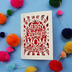 Laser cut Mom Card with 'Merry Christmas to my Mom' text surrounded by colourful pom-poms on a blue background