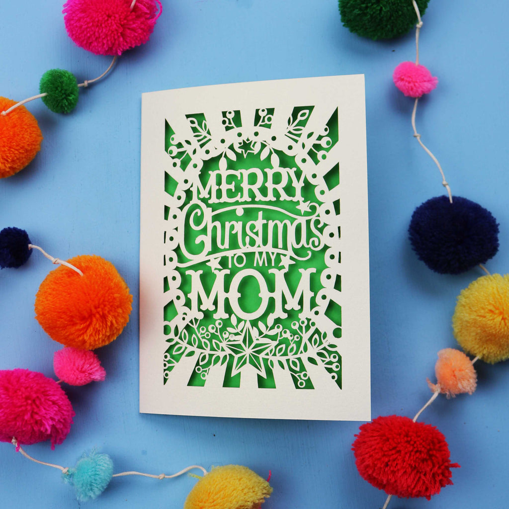 Laser cut Mom Card with 'Merry Christmas to my Mom' text surrounded by colourful pom-poms on a blue background