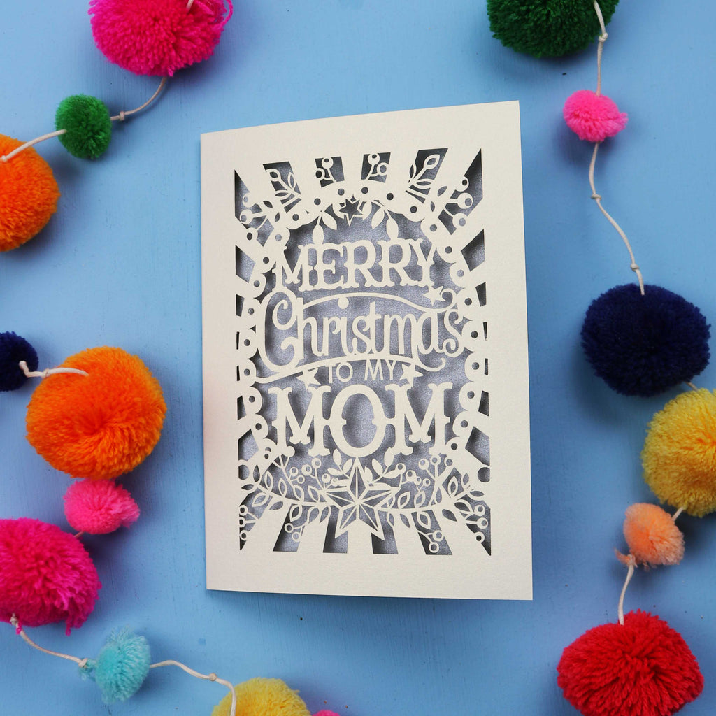 Laser cut Mom Card with 'Merry Christmas to my Mom' text surrounded by colourful pom-poms on a blue background