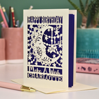 A personalised Birthday card with laser cut crescent moon design and text, 'Happy Birthday, Make a Wish Charlotte', on a desk with stationery items.