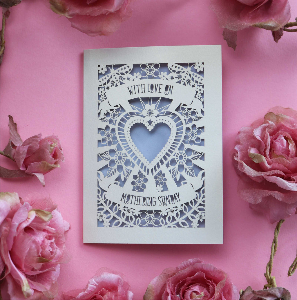 A cream cut out Mother's Day card that says "With love on Mothering Sunday". Card has a heart and flower details and a lilac paper insert