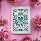 A cream laser cut Mothering Sunday card that says "With love on Mothering Sunday". Card has a heart and flower details and a sage paper insert