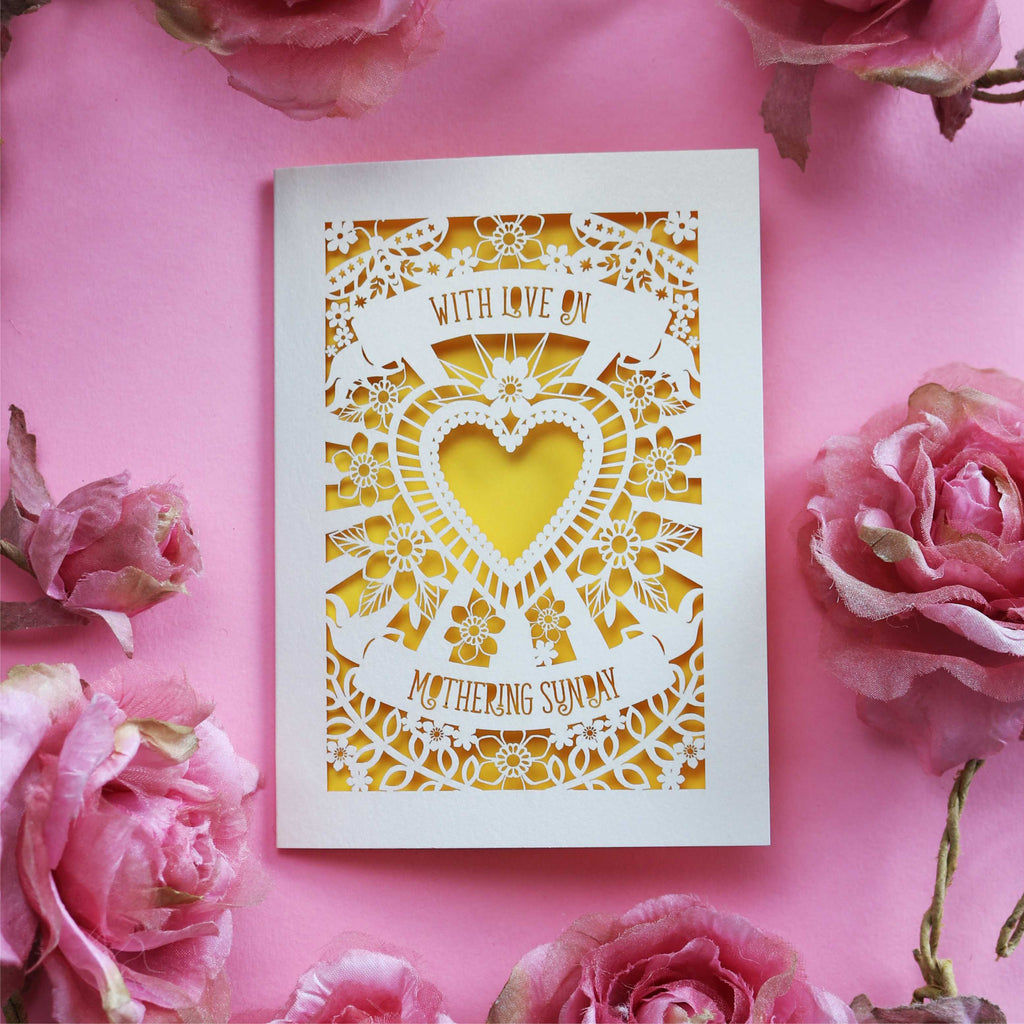 A cream laser cut Mothering Sunday card that says "With love on Mothering Sunday". Card has a heart and flower details and a yellow paper insert