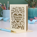 Laser-cut Mrs and Mrs anniversary card with personalized text, 'Mrs and Mrs Butler-Woods, 01/05/25', surrounded by leaves and flowers,  on a desk with stationery items.