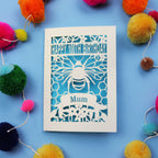 Paper cut 100th birthday card for 'Mum' with bee design on a blue background with colourful pom-poms.