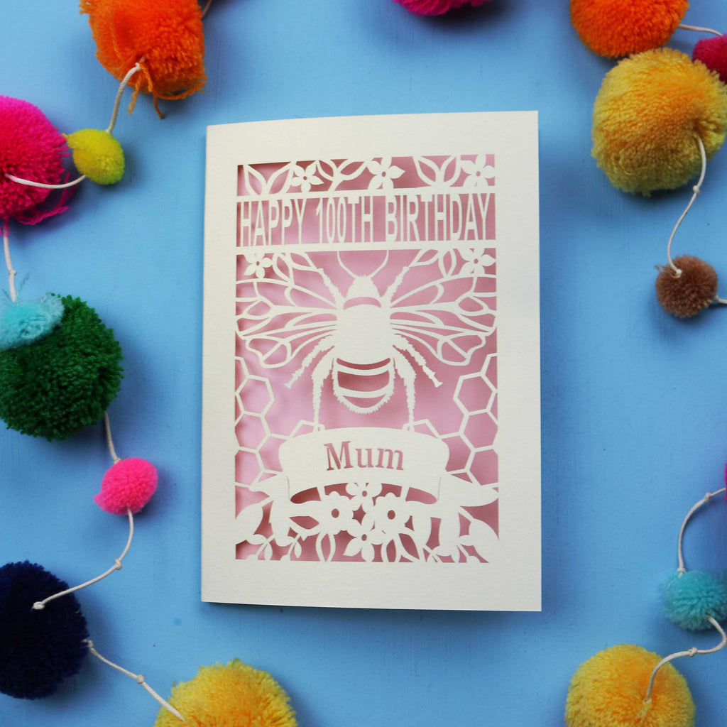 Laser-cut 100th birthday card for 'Mum' with bee design on a blue background with colourful pom-poms.