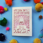 Laser-cut 100th birthday card for 'Mum' with bee design on a blue background with colourful pom-poms.
