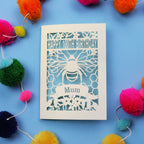 Laser-cut 100th birthday card for 'Mum' with bee design on a blue background with colourful pom-poms.